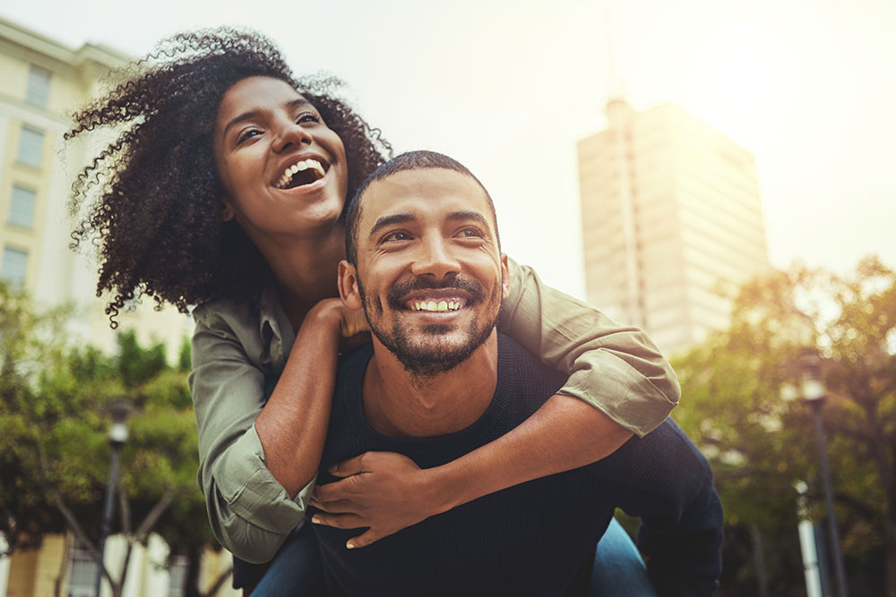 A smiling couple shares a piggy back ride, showing the benefits of relationship counseling and dating therapy in Buckhead, GA