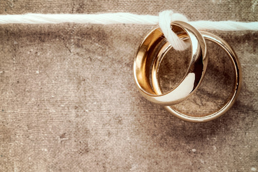 Wedding rings hanging on rope over a dirty canvas background. This image symbolizes the bond that's created during Atlanta premarital counseling.