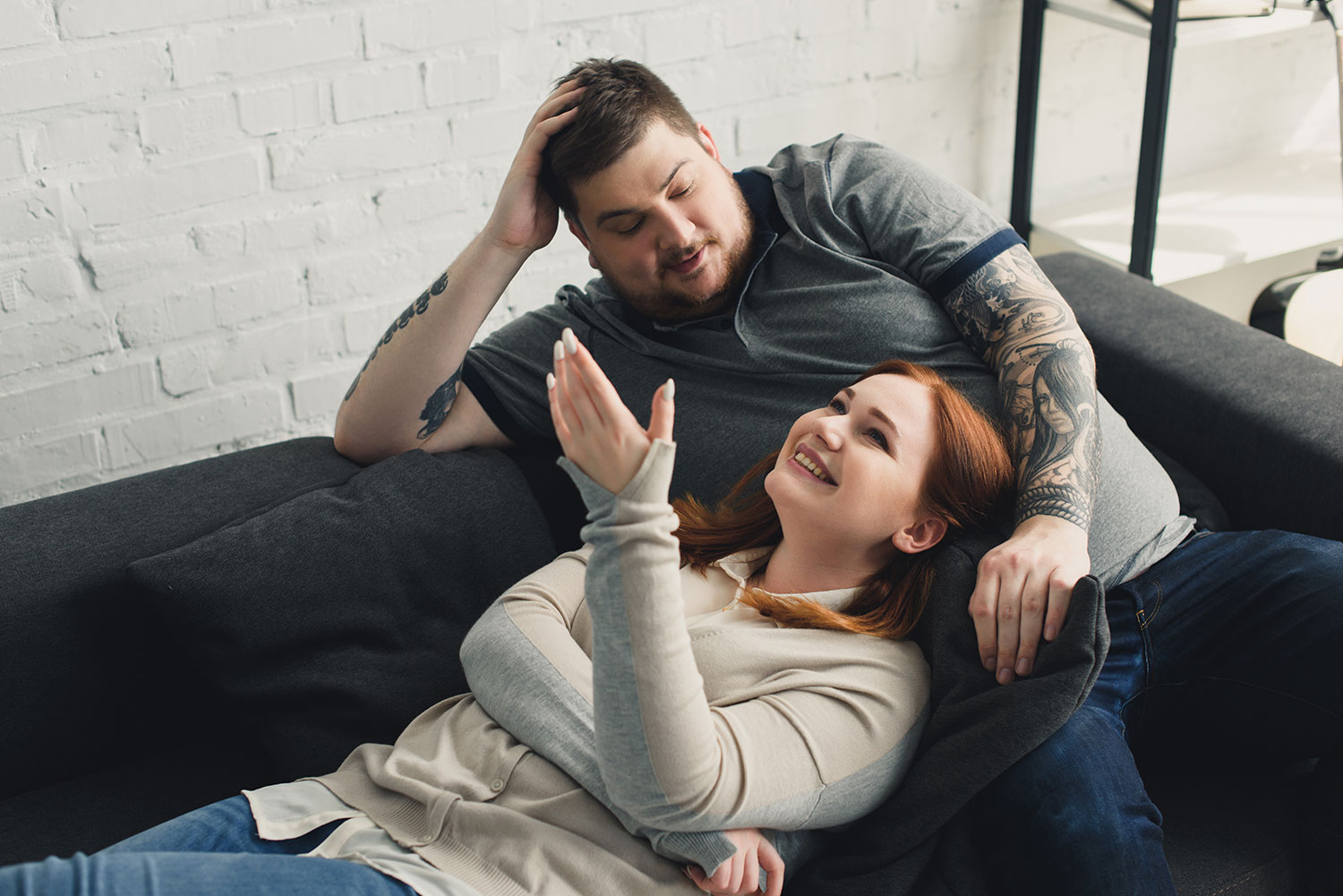 A married couple is seated on a cozy couch, their smiles radiating happiness. The wife's head rests gently in her husband's lap, showcasing the comfort and intimacy between them. This heartwarming scene captures the positive outcome of their journey through Atlanta marriage counseling, where they have found renewed joy and connection in their relationship. Their beaming expressions are a testament to the success of their therapeutic endeavors, which have rekindled the spark in their marriage.